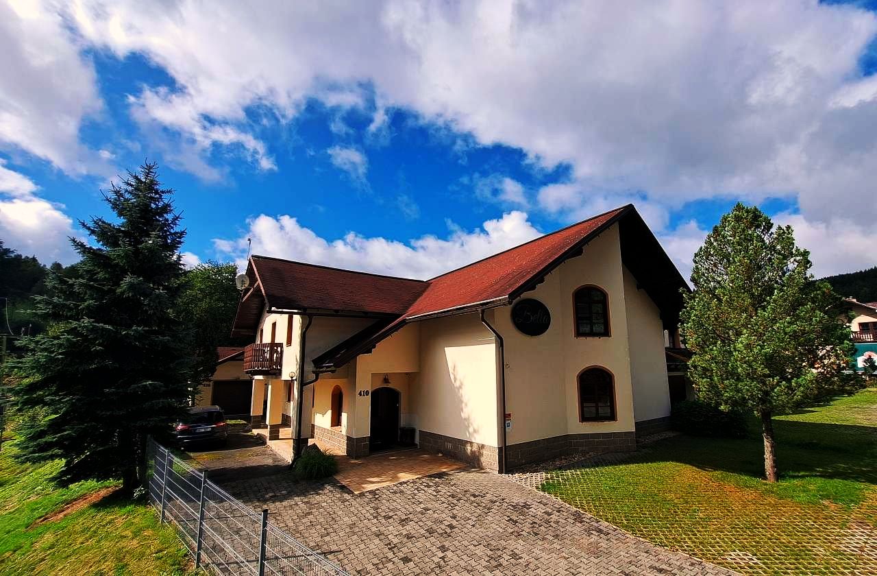 Penzion Bella v létě — fasáda s hrázděným štítem, trávník a smrky